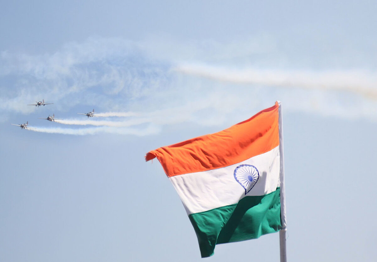 The Indian national flag flying with a formation of aircraft passing in the sky behind it
