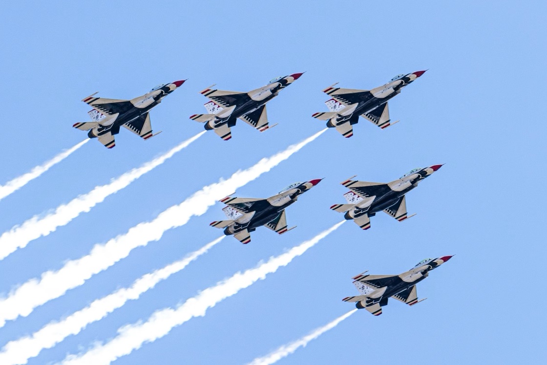 Six aircraft climbing together in formation, each trailing a straight white smoke line