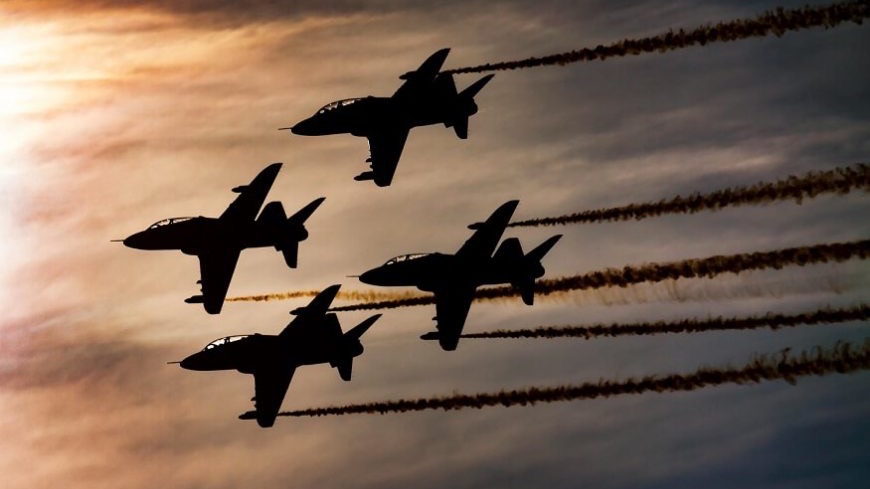 Four aircraft in tight formation silhouetted against a low sun, trailing smoke