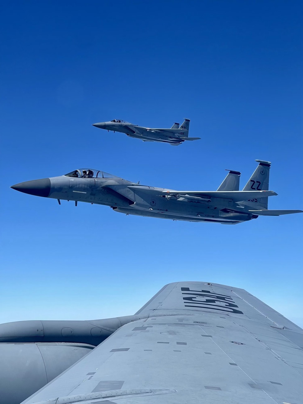 Fighter aircraft flying in formation alongside a larger aircraft's wing, viewed from above