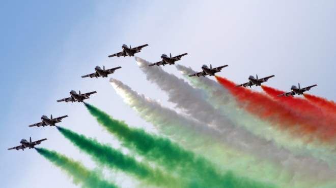 A large formation of aircraft flying in close order while trailing green, white and red smoke
